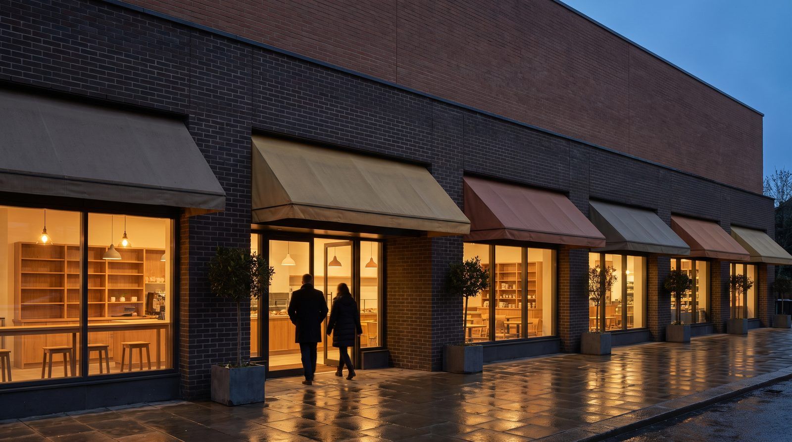 Row of lit, occupied shops at dusk with awnings and warm interiors