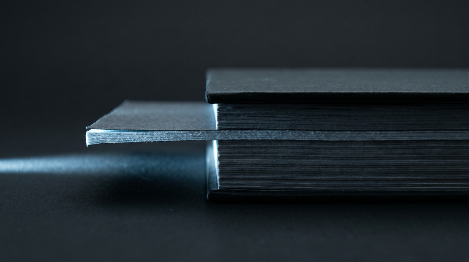 Dark technical documents edge on, one page catching the light